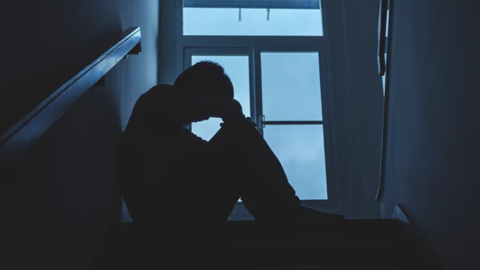 a man with substance use disorder holds his head in his hand at the top of a staircase