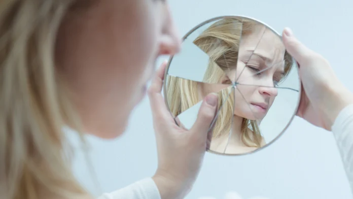A woman looks at a shattered reflection of herself in a mirror