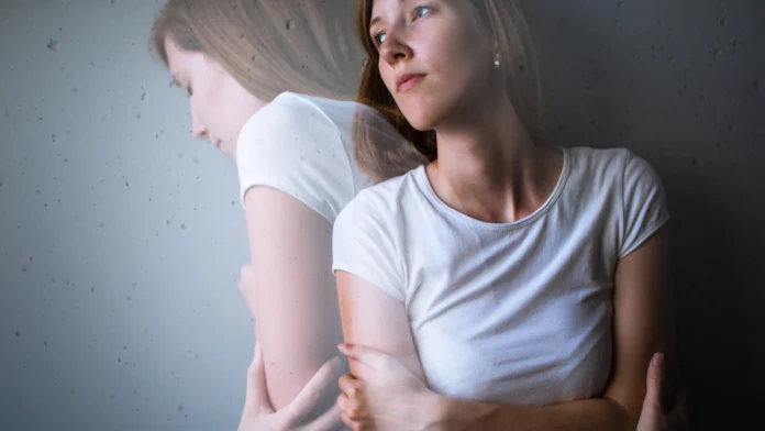 A depressed looking woman leans against a wall, back to back with an image of herself
