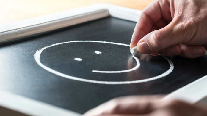 A person draws a smiley face onto a chalkboard