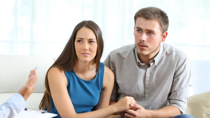 An anxious couple holds hands while speaking with a doctor