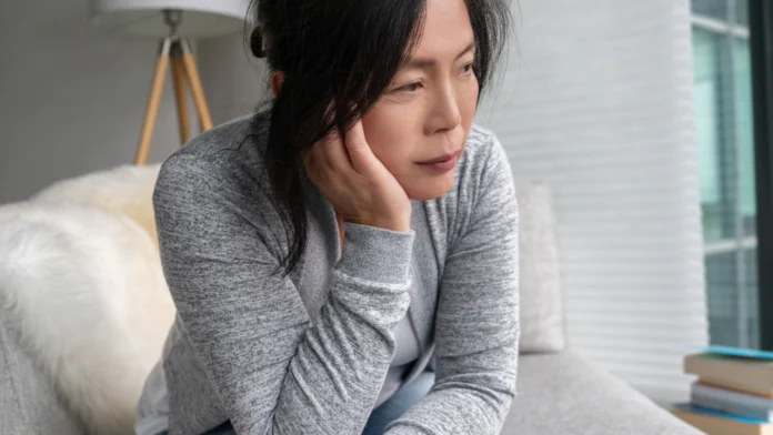 A sad-looking woman sits on a couch while looking off into the distance