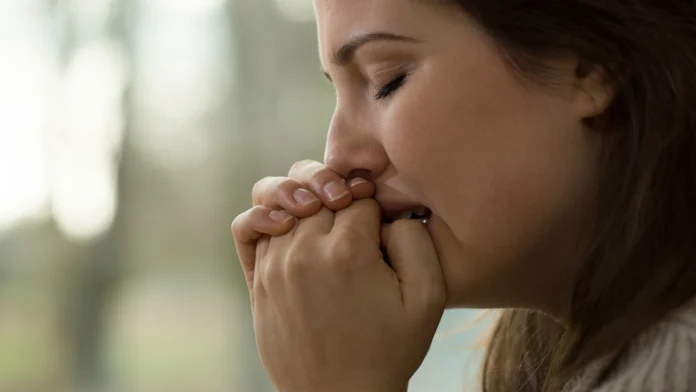 A distressed woman clasps her hands together with her eyes closed