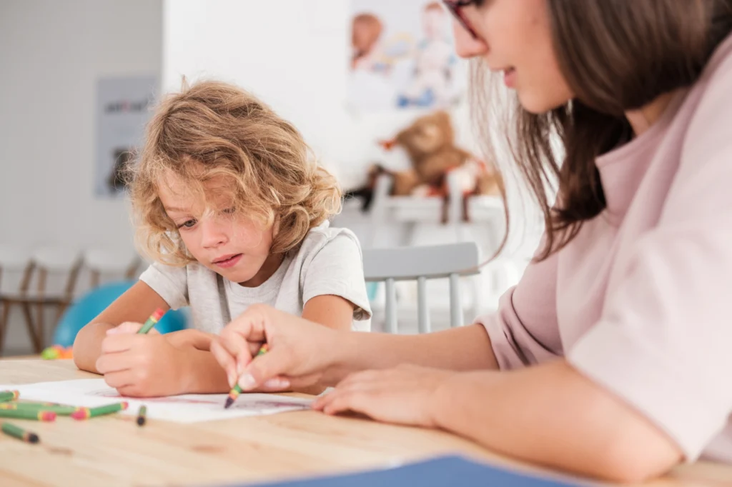 A child draws on a piece of paper while an adult watches