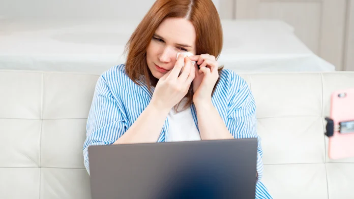 A woman cries while looking at a laptop