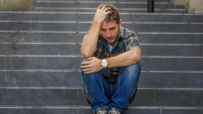 A depressed man rubs his head while sitting on a staircase
