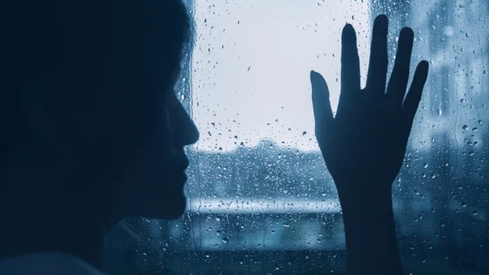 A person places their hand on a wet window while it rains