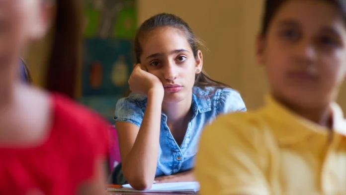 A sad-looking child disassociates at the back of a classroom
