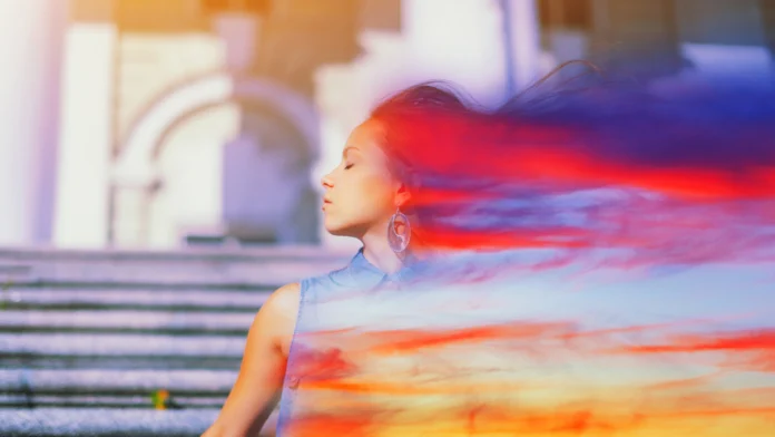 A radiant woman standing in front of a staircase, with color flowing off of her. Learn how ERP therapy can help treat your OCD here.