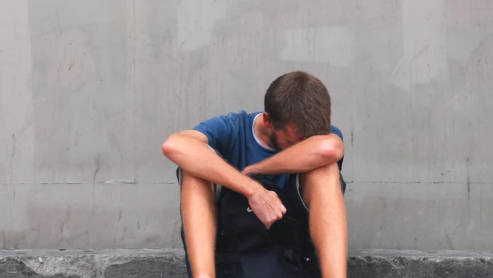 A man sits on the ground, looking depressed. Therapy for sex addiction can improve your mental well-being.