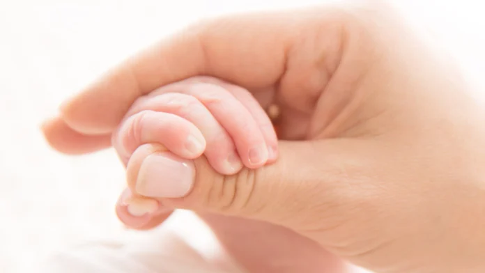 A mother holds the hand of her baby. Therapy for postpartum mood swings can make the early days of parenthood more manageable.