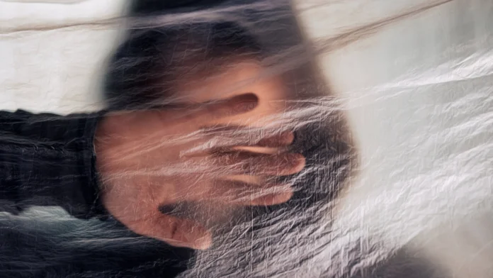 A man holds a hand in front of his face, obscuring it