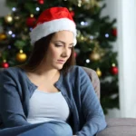 A woman afflicted by holiday depression, sitting in front of a Christmas tree