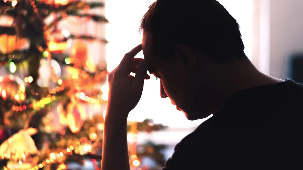 A man clutches his forehead, afflicted by the holiday blues