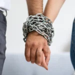 A couple holding hands with chained together wrists, suggesting codependency or a dysfunctional relationship