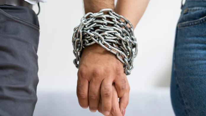 A couple holding hands with chained together wrists, suggesting codependency or a dysfunctional relationship