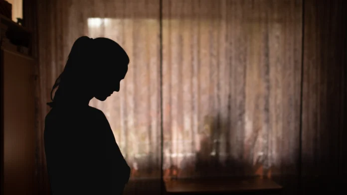 A dark photo of a sad woman. Learn more about abuse, including types, effects, signs, and how therapy can help, here.