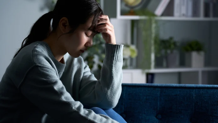 A depressed woman grips her forehead. Learn more about physical abuse, including signs, effects, and how to get help, here.