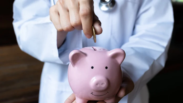 A doctor deposits a coin into a piggy bank. Learn more about the real cost of therapy, and what most people pay for treatment, here.