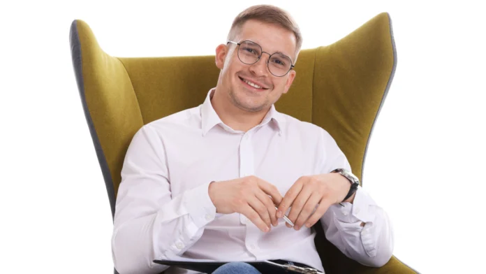 A therapist sitting in a chair against a white background. Learn more about therapy resources here.